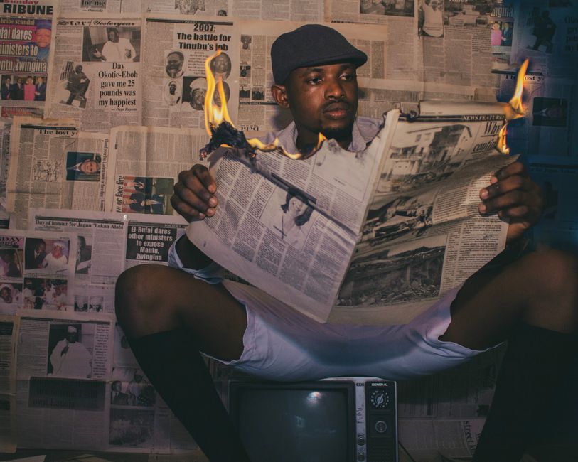 A man reads a burning newspaper in a classic room with vintage decor and a retro TV.