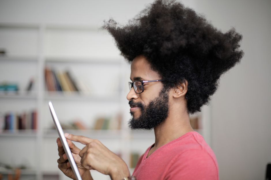 Side view profile of a black man with an afro using a tablet in a room full of books.